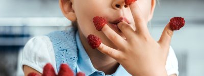 cute happy kid sitting at table and eating ripe fresh raspberries